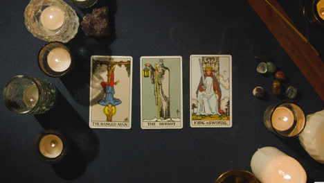 Overhead-Shot-Of-Person-Giving-Tarot-Card-Reading-Laying-Down-The-Hermit,-The-King-Of-Swords-And-The-Hanged-Man-Cards-On-Table